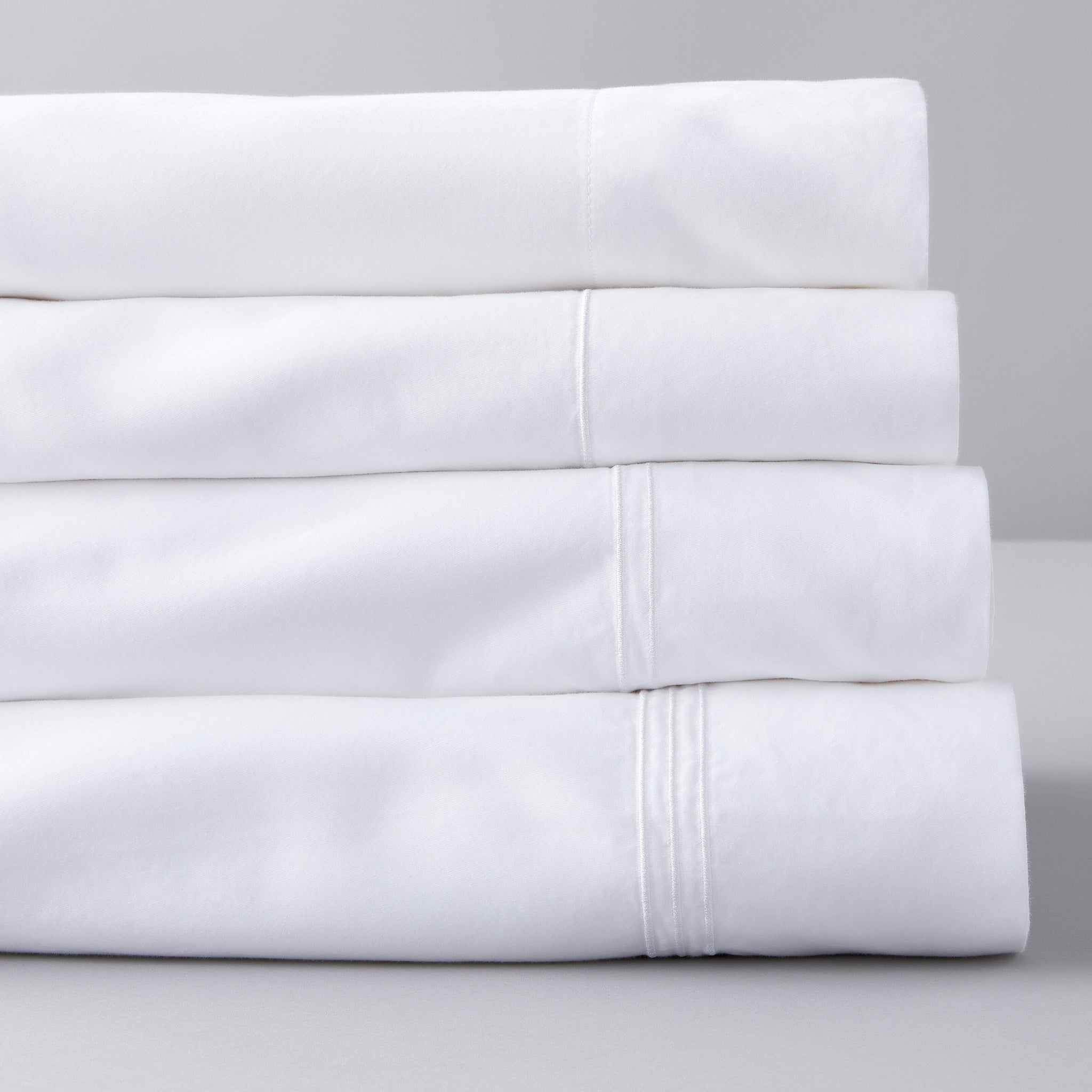 stack of white sheets. Bottom sheet is a king sheet with 3 lines of embroidery, above that is a queen sheet with 2 lines of embroidery, above that is a full sheet with one line of embroidery and above that is a twin sheet with no embroidery