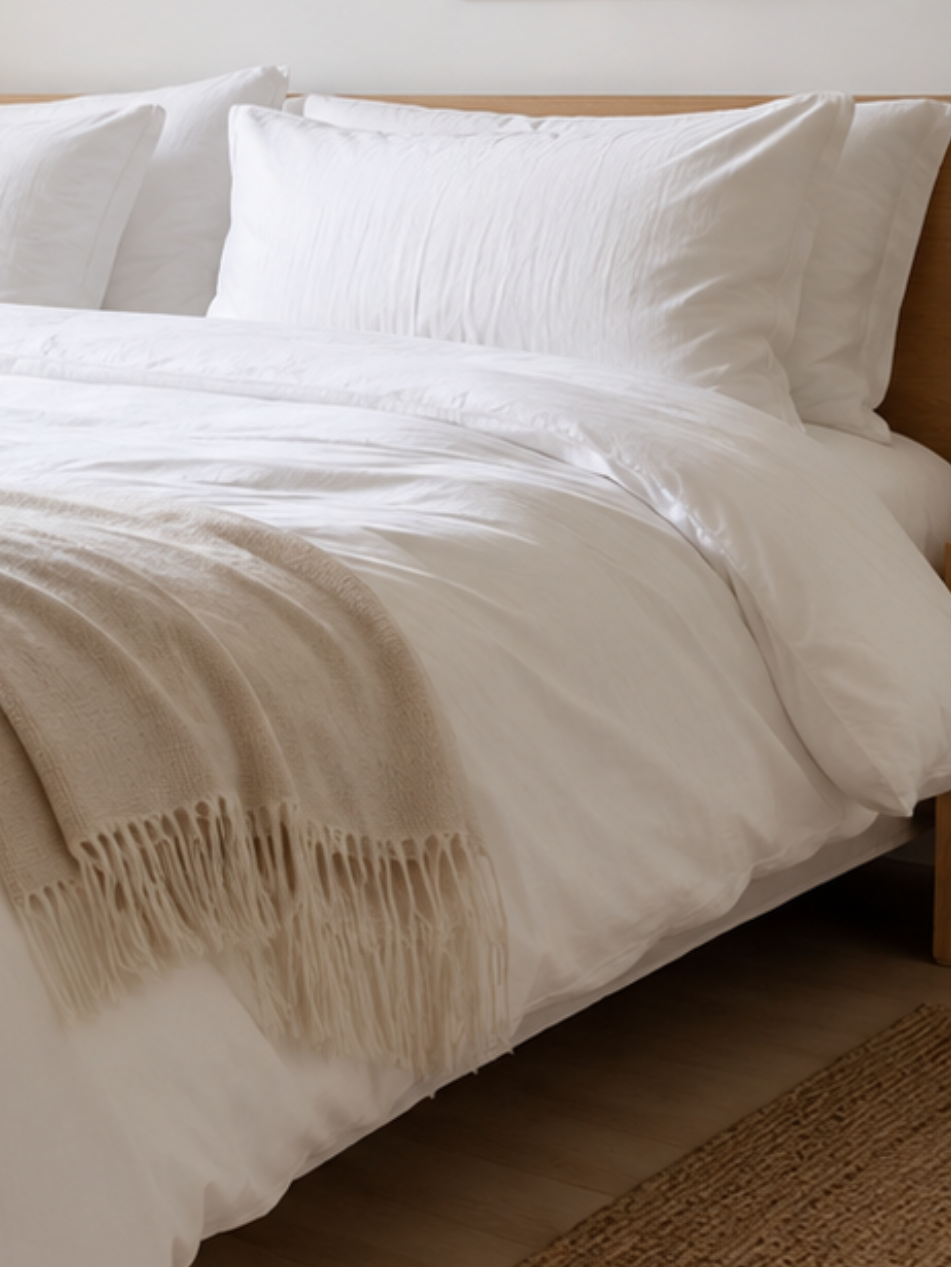 Neatly made bed with white bedding and a wooden headboard in a bedroom setting.