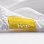 fix linens simple sort sheets. close up of fitted sheet with yellow tag making twin size and top center